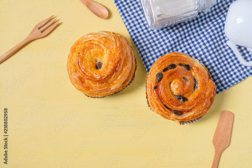 Raisin danish pastry on the yellow wood and blue gingham check cloth. Colourful tasty sweet bakery..