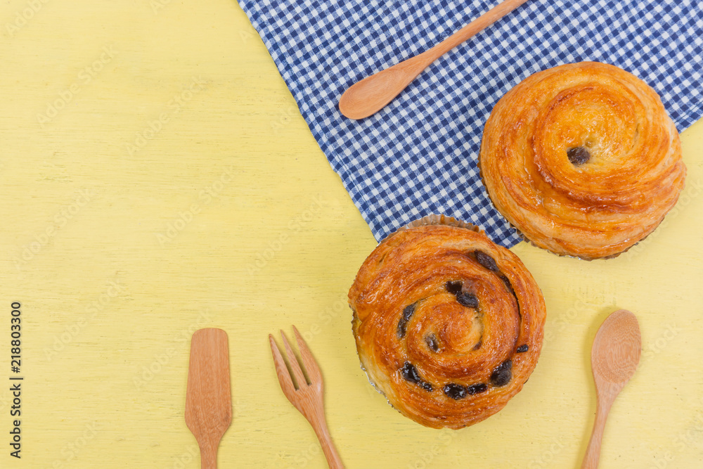Raisin danish pastry on the yellow wood and blue gingham check cloth. Colourful tasty sweet bakery..