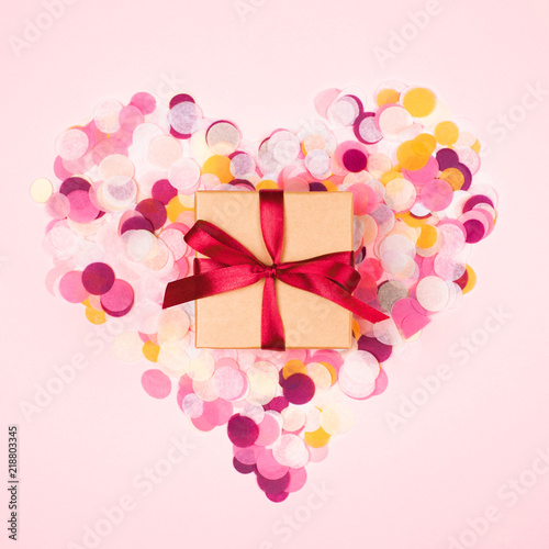 Kraft gift box tied with red bow on pink background decorated with confetti i...