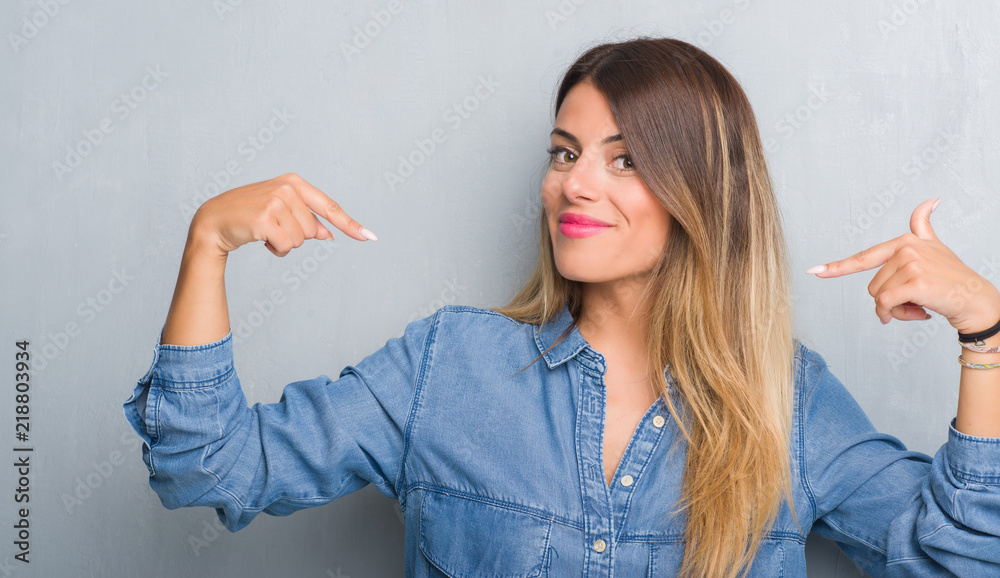 Young adult woman over grunge grey wall wearing denim outfit looking confident with smile on face, pointing oneself with fingers proud and happy. - obrazy, fototapety, plakaty 