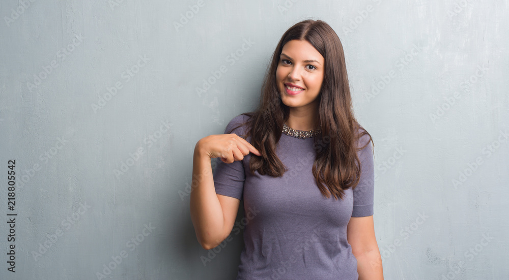 Young brunette woman over grunge grey wall with surprise face pointing finger to himself