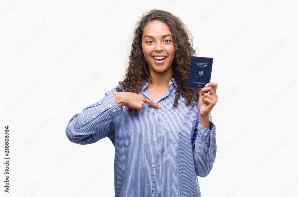 Young hispanic woman holding passport of Germany with surprise face pointing finger to himself Young hispanic woman holding passport of Germany with surprise face pointing finger to himself
