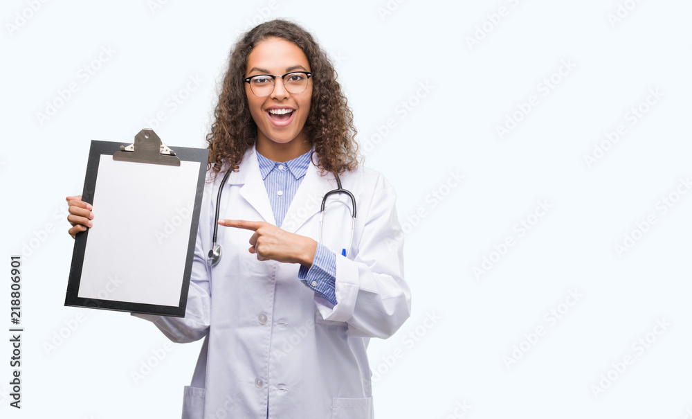 Young hispanic doctor woman holding a clipboard very happy pointing with hand and finger Young hispanic doctor woman holding a clipboard very happy pointing with hand and finger