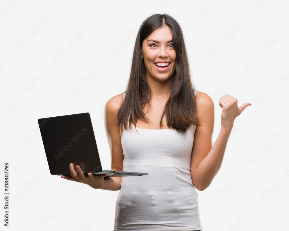Young hispanic woman using computer laptop pointing and showing with thumb up to the side with happy face smiling Young hispanic woman using computer laptop pointing and showing with thumb up to the side with happy face smiling