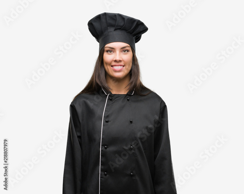 Young hispanic cook woman wearing chef uniform with a happy face standing and smiling with a confident smile showing teeth