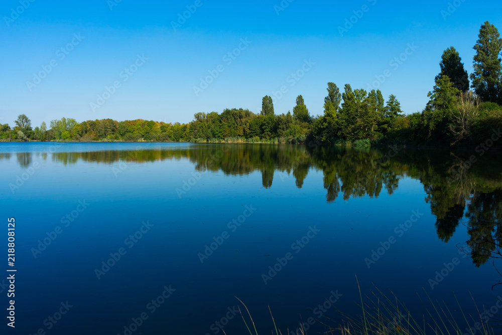 kleiner See mit Bäumen am Ufer bei blauem Himmel