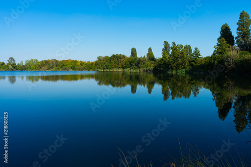 kleiner See mit Bäumen am Ufer bei blauem Himmel