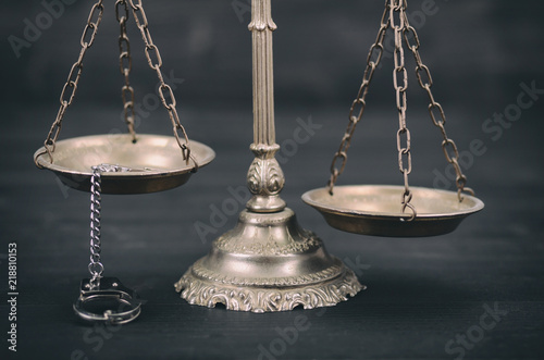 Scales of Justice and handcuffs on a black wooden background.