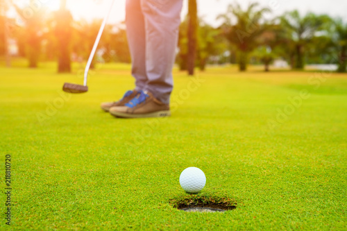 Golfer putting golf ball on the green golf, lens flare on sun set evening time, Pro Golf long putting golf ball in to the hole, sunset scene time.