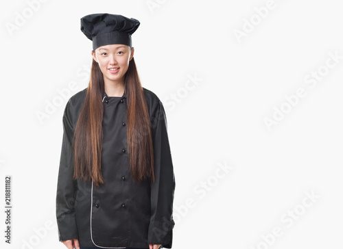 Young Chinese woman over isolated background wearing chef uniform with a happy and cool smile on face. Lucky person.