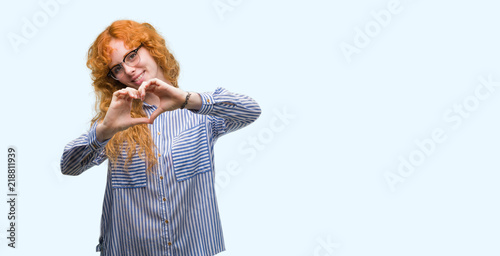 Young redhead bussines woman smiling in love showing heart symbol and shape with hands. Romantic concept.