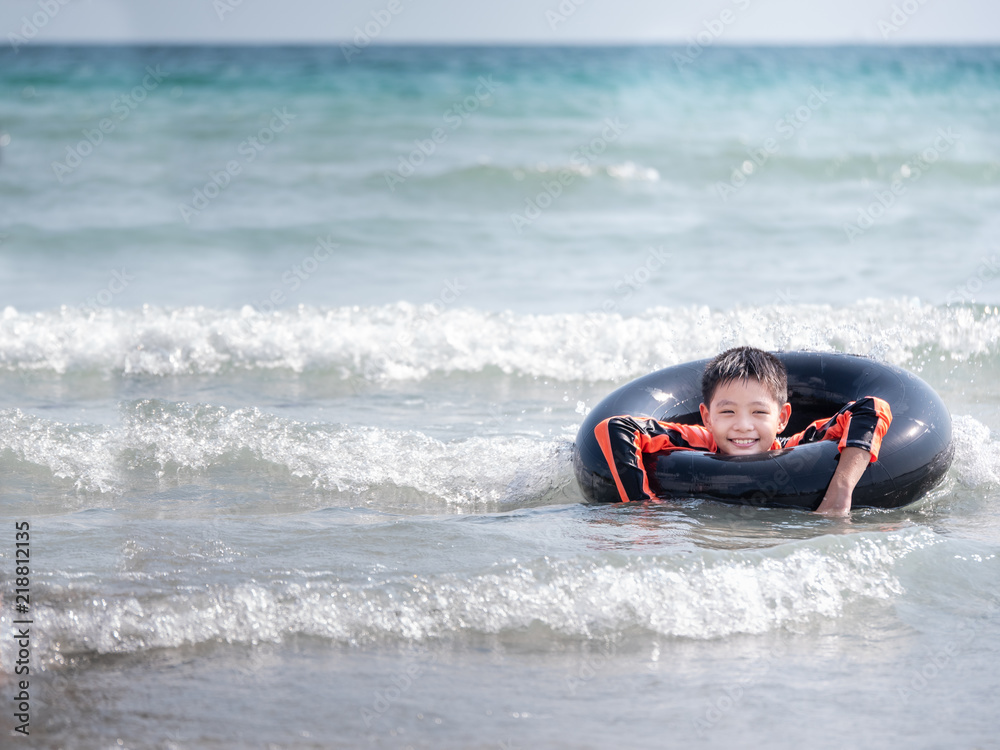 little Asian boy play waves on the beach , with a lifebuoy little Asian boy play waves on the beach , with a lifebuoy