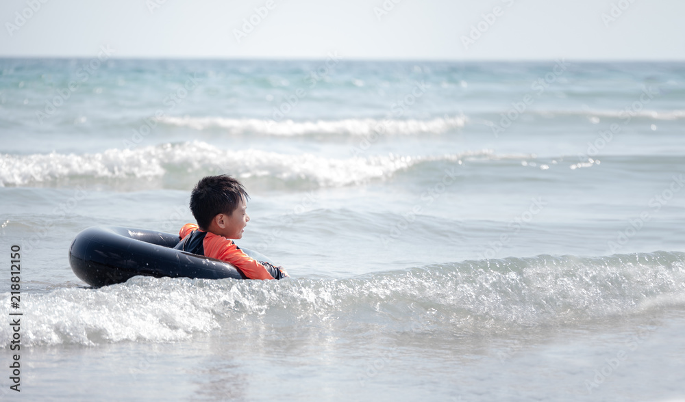 little Asian boy play waves on the beach , with a lifebuoy little Asian boy play waves on the beach , with a lifebuoy
