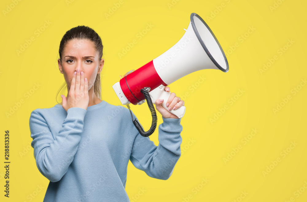 Beautiful young woman holding megaphone cover mouth with hand shocked with shame for mistake, expression of fear, scared in silence, secret concept Beautiful young woman holding megaphone cover mouth with hand shocked with shame for mistake, expression of fear, scared in silence, secret concept