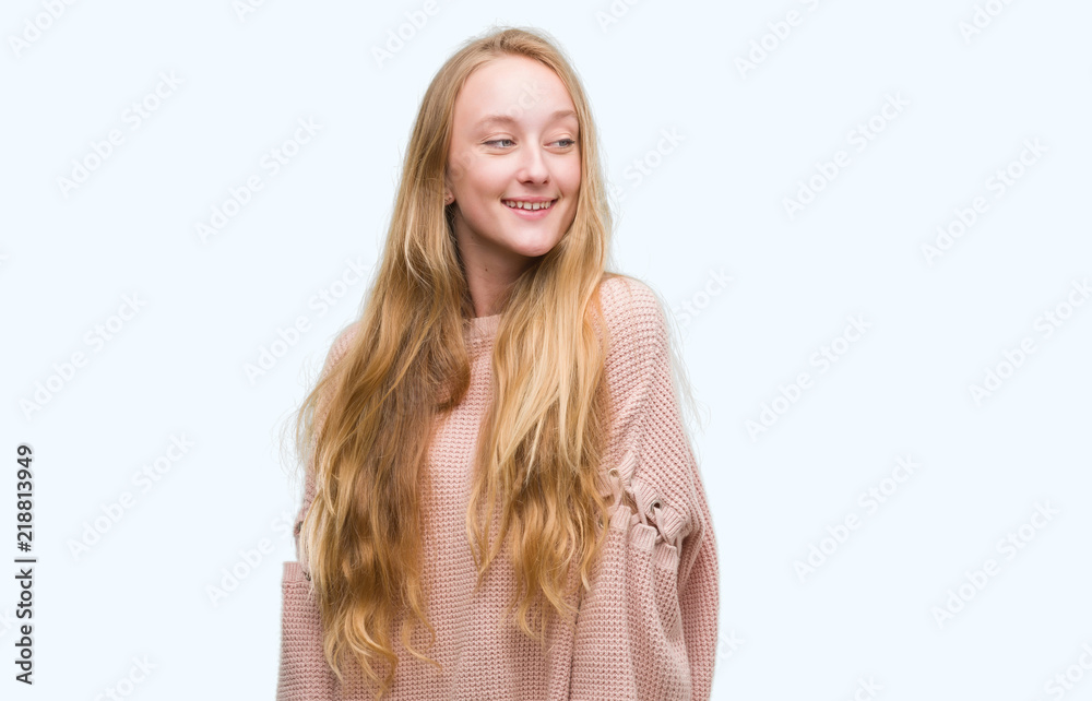 Blonde teenager woman wearing pink sweater looking away to side with smile on face, natural expression. Laughing confident.