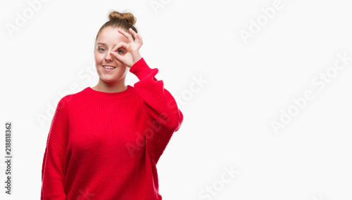 Young blonde woman wearing bun and red sweater doing ok gesture with hand smiling, eye looking through fingers with happy face.