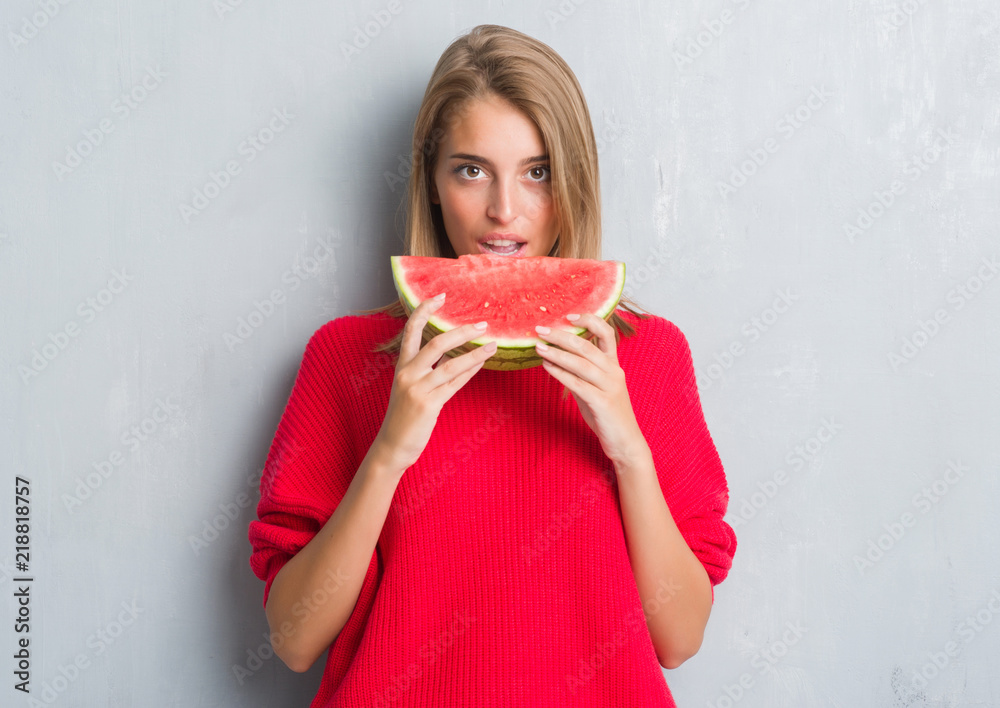 Beautiful young woman over grunge grey wall eating water melon with a confident expression on smart face thinking serious