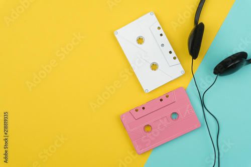 top view of the white and pink audio cassette tapes and a black headphone on the yellow and blue background
