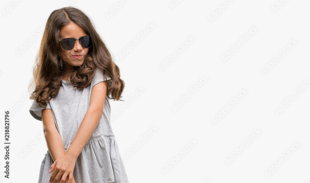 Fototapeta premium Brunette hispanic girl wearing sunglasses looking away to side with smile on face, natural expression. Laughing confident.