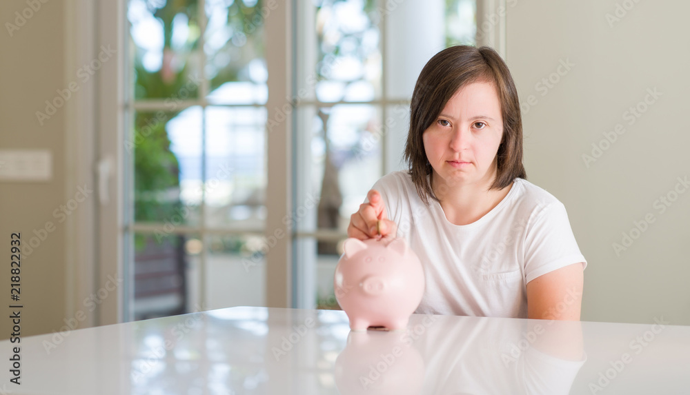 Down syndrome woman at home holding piggy bank with a confident expression on smart face thinking serious Down syndrome woman at home holding piggy bank with a confident expression on smart face thinking serious