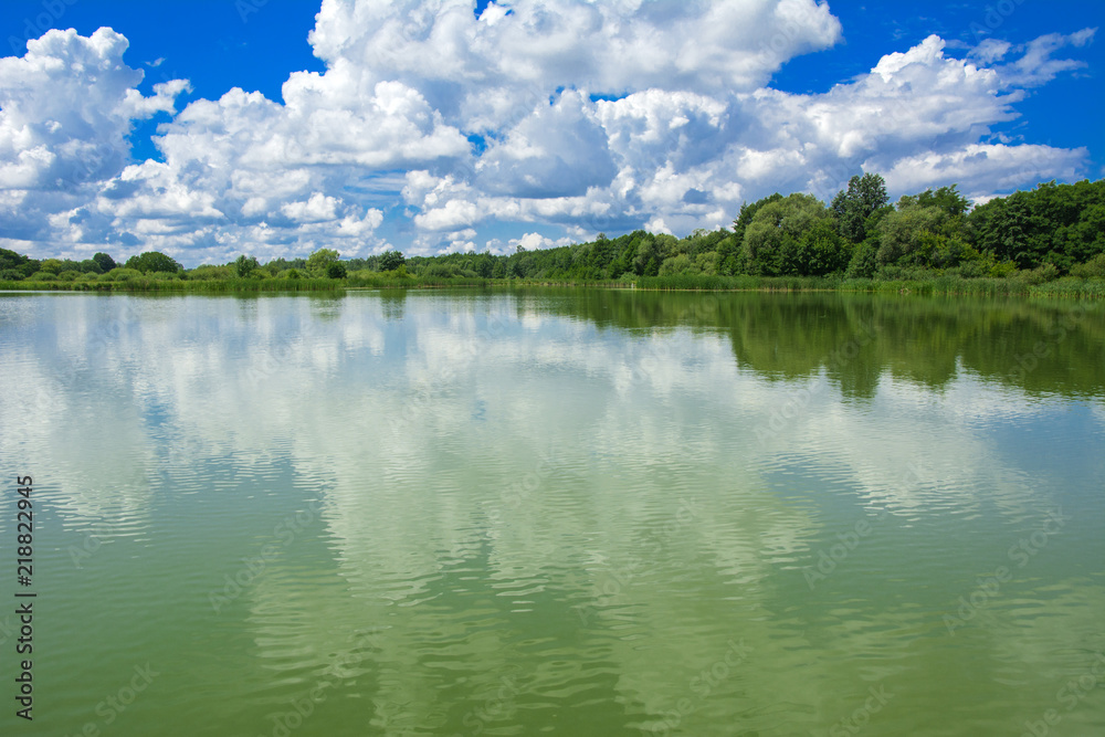 A beautiful image of landscape from the center of the river, surrounded by trees and reeds on the shore and distant horizon against the blue sky in clouds. Reflection, water, tourist destination