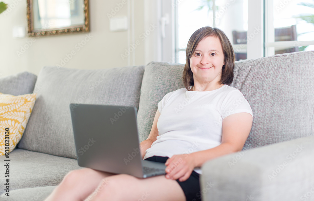 Down syndrome woman at home using computer laptop with a happy face standing and smiling with a confident smile showing teeth Down syndrome woman at home using computer laptop with a happy face standing and smiling with a confident smile showing teeth