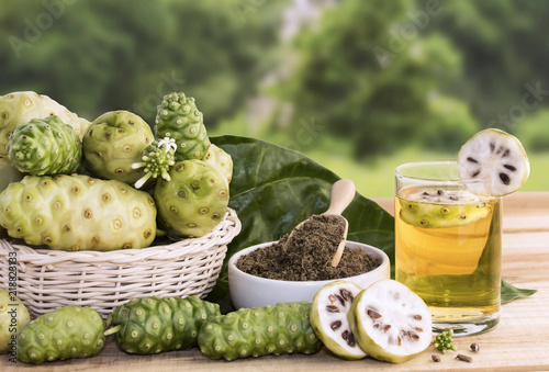 Noni fruit juice or Morinda Citrifolia with noni slice and noni powder for health on the wooden background with copy space for text.