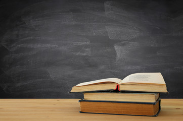 back to school concept. stack of books over wooden desk in front of blackboard.