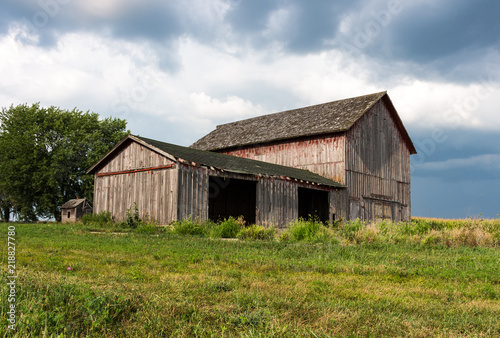 Abandoned farm with old painted red barns standing empty on a hill with dark clouds. Gives the feeling of trouble, a storm brewing for farmers. Concepts of family farm, trade wars, tariffs