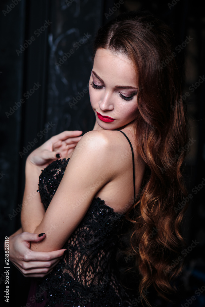 Young woman with long curly hair and makeup in evening long luxury dress, posing in a dark interior room. fashion beauty portrait Young woman with long curly hair and makeup in evening long luxury dress, posing in a dark interior room. fashion beauty portrait