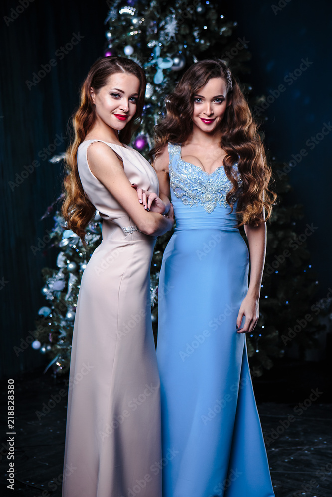 Twins young women in evening dresses over christmas background, fashion beauty portrait in dark interior