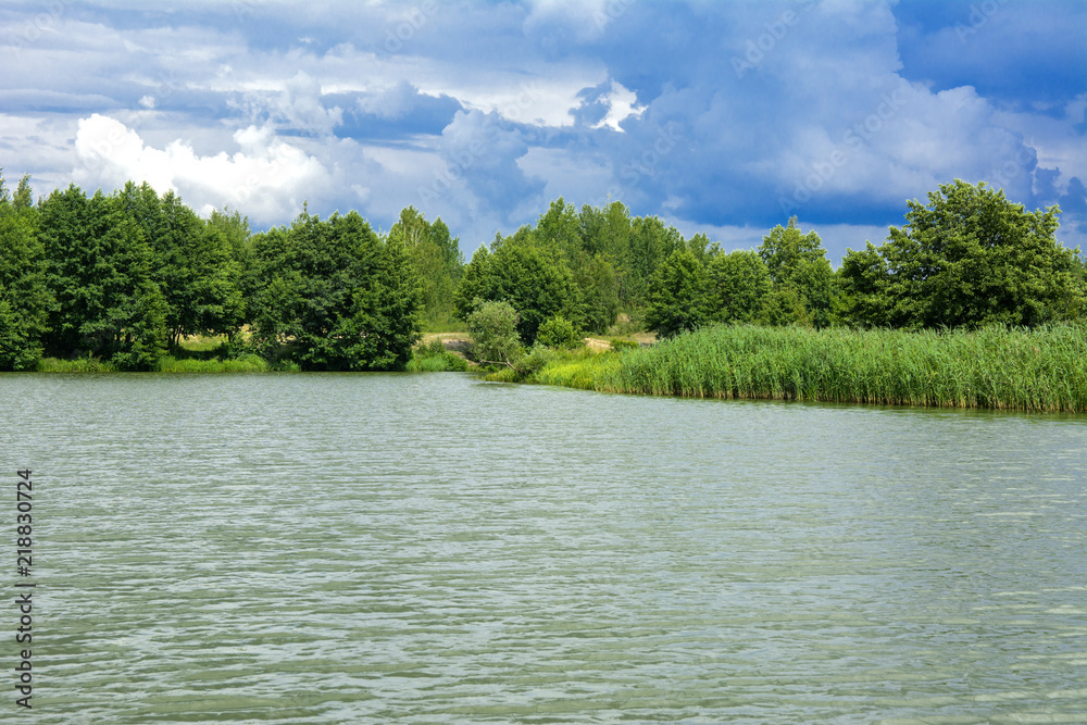 Fototapeta premium A beautiful image of landscape from the center of the river, surrounded by trees and reeds on the shore and distant horizon against the blue sky in clouds. Reflection, water, tourist destination
