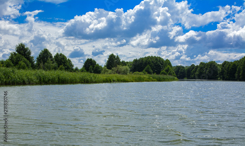 A beautiful image of landscape from the center of the river  surrounded by trees and reeds on the shore and distant horizon against the blue sky in clouds. Reflection  water  tourist destination
