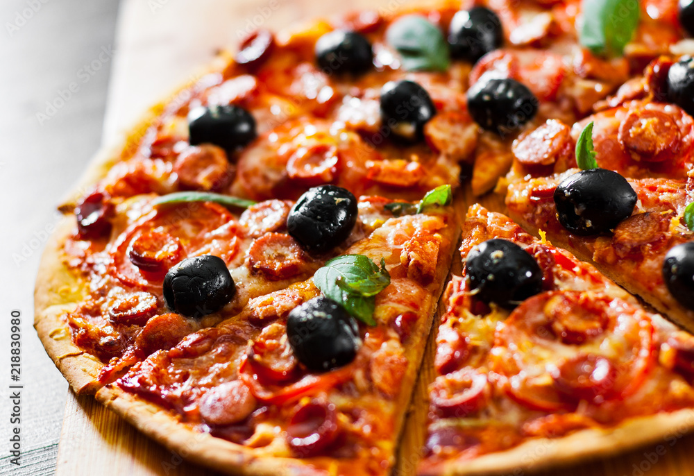 slices of Pizza with Mozzarella cheese, salami, pepper, pepperoni, Tomatoes, olives, Spices and Fresh Basil. Italian pizza on wooden background