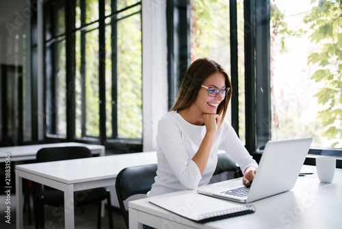 Portrait of smiling student looking at laptop in modern study room.