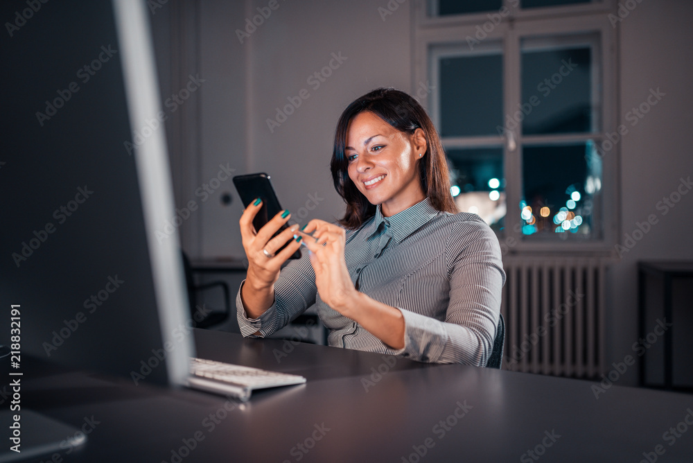 Charming businesswoman using smartphone while working late.