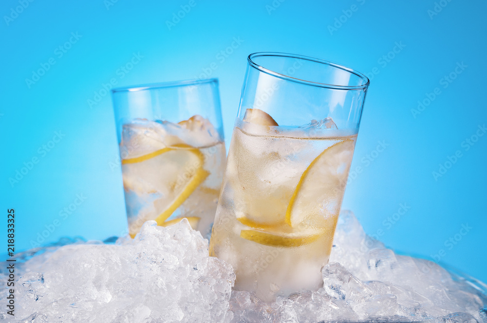 Two glasses with a drink with ice with pieces of lemon in a pile of ice. Light blue background. Two glasses with a drink with ice with pieces of lemon in a pile of ice. Light blue background.