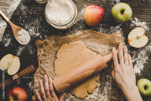 Preparing pie crust for apple pie. Hands rolling dough with rolling pin on the wooden background