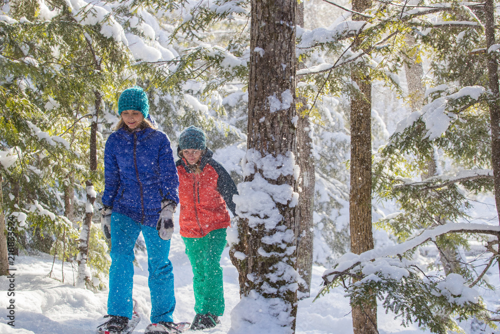 Pair of female friends snowshoeing in forest.