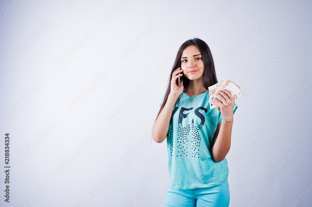 Portrait of an attractive girl in blue or turquoise t-shirt and trousers posing with a lot of money and smartphone in her hands.