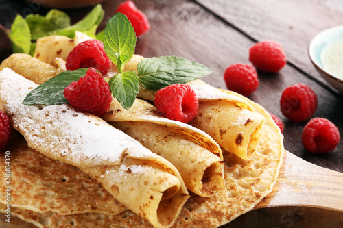 Homemade crepes served with fresh raspberrries and powdered sugar on rustic table.