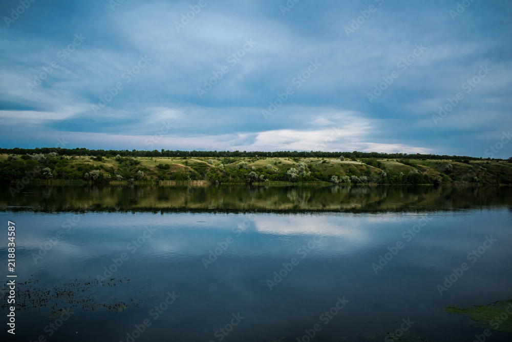 A simple landscape in the Rostov region in Russia, the river - Seversky Donets, Don. Spring is the beginning of summer. Green vegetation, trees. Cool fresh lake water. Colorful sky and its reflection 