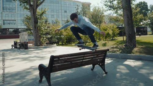 Skater doing ollie jump trick on over bench in skatepark, street skate trick gap slow motion