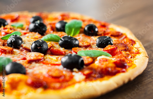 Pizza with Mozzarella cheese, salami, pepper, pepperoni, Tomatoes, olives, Spices and Fresh Basil. Italian pizza on wooden background
