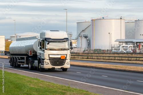 Tanker lorry in motion on the road and fuel terminal in the background