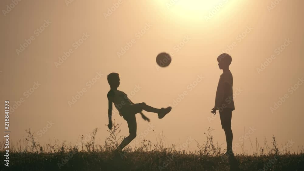 Two boys playing soccer at sunset. Silhouette of children playing with a ball at sunset. The concept of a happy family Two boys playing soccer at sunset. Silhouette of children playing with a ball at sunset. The concept of a happy family