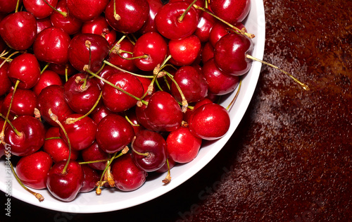 Pile of fresh cherries in the white bowl on the table top angle background