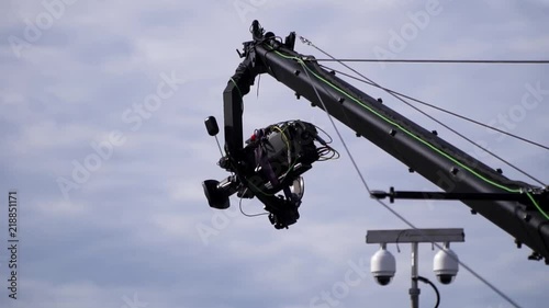 Broadcast TV camera on a moving jimmy jib crane arm, next to surveillance cctv cameras at a outdoor event
(slow motion)