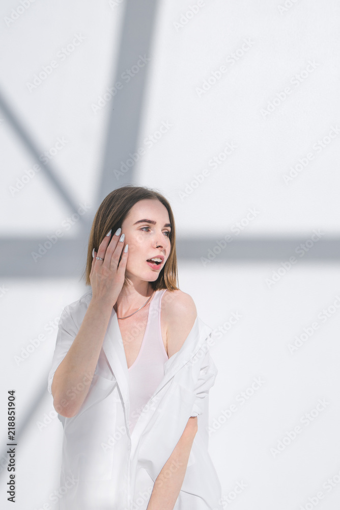 Attractive woman in white clothes poses against the background of a light wall with shadows. Fashionable photo of a stylish woman in fashionable clothes. Attractive woman in white clothes poses against the background of a light wall with shadows. Fashionable photo of a stylish woman in fashionable clothes.