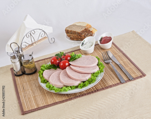 Sliced boiled sausages with tomatoes on lettuce leaves are laid on a plate.